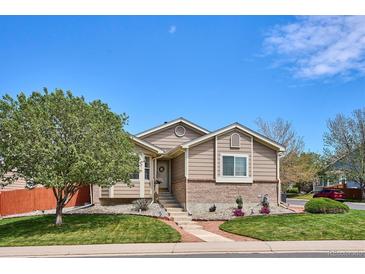 Charming single Gathering home showcasing a well-manicured lawn, mature tree, and inviting brick accents beneath neutral siding at 18477 E Amherst Dr, Aurora, CO 80013