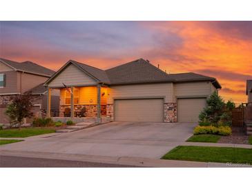 Charming home with a two-car garage, covered porch, stone accents, and beautiful landscaping during sunset at 19468 E 65Th Pl, Aurora, CO 80019