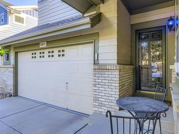 Home exterior with a two-car garage, brick details, front door, and small outdoor seating area at 11811 Lewiston St, Commerce City, CO 80022