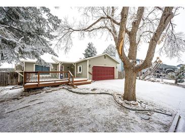 Charming home featuring a spacious wooden deck, red garage door and snow-covered front yard with mature trees at 4274 S Fundy Way, Aurora, CO 80013