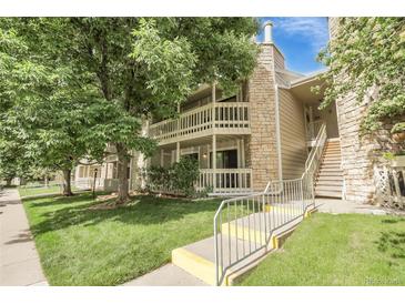 Inviting two-story condo featuring a charming balcony, stone accents, and lush green landscaping at 8225 Fairmount Dr # 102, Denver, CO 80247