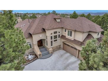 Elegant stucco home featuring a three-car garage, complemented by lush pine trees, blue sky, and distant mountain views at 9132 Scenic Pine Dr, Parker, CO 80134