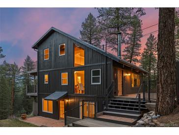 Two-story home featuring a black facade, multi-level deck, and surrounded by mature trees at sunset at 27891 Columbine Rd, Evergreen, CO 80439