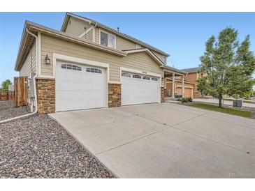 Home exterior featuring a three-car garage, concrete driveway, stone accents, and well-maintained landscaping at 56579 E 23Rd Pl, Strasburg, CO 80136