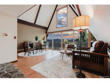 Inviting living room with vaulted ceilings and a wall of windows offering stunning mountain views at 8691 S Warhawk Rd, Conifer, CO 80433