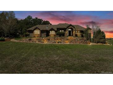 Charming exterior featuring a stone facade and manicured landscaping with a retaining wall at sunset at 19336 Queens Crescent Way, Monument, CO 80132