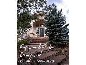 Inviting front entrance with brick steps leading to a modern, light colored home with large windows and mature trees at 1425 Autumnwood Ln, Evergreen, CO 80439