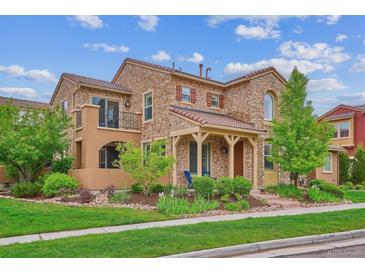 Charming two-story stone home featuring a manicured lawn and inviting covered porch at 9528 Pendio Ct, Highlands Ranch, CO 80126