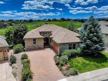 Beautiful exterior of home with stone accents, brick driveway, and lush landscaping and view of the golf course and blue sky at 11208 W Ontario Ave, Littleton, CO 80127