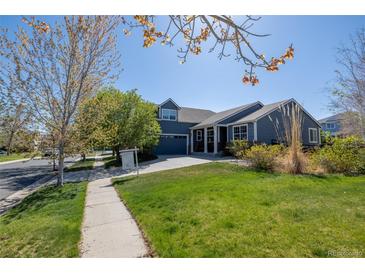Charming blue home with a well-manicured lawn, mature trees, and a paved walkway leading to the entrance at 275 Gold Maple St, Brighton, CO 80601