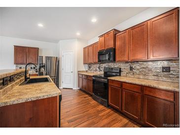 Well-lit kitchen features wood cabinets, stainless steel appliances, tile backsplash and wood flooring at 1788 Taos St, Brighton, CO 80603
