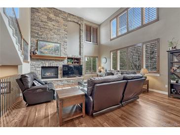 Cozy living room with a stone fireplace, hardwood floors, and plentiful windows to allow lots of natural light at 8707 Windhaven Dr, Parker, CO 80134