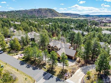 Stunning aerial view of a home nestled among trees with mountain backdrop and adjacent golf course at 648 Ruby Trust Dr, Castle Rock, CO 80108