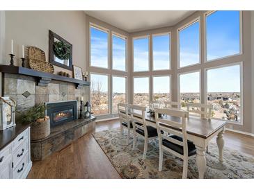 Bright dining area with a stone fireplace, large windows, and hardwood floors create an inviting and elegant space at 12007 W 54Th Dr, Arvada, CO 80002