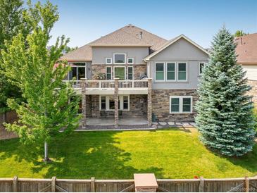 A two-story home showcasing a lush backyard, a stone patio, and a charming balcony on the second story at 13943 W 87Th Ln, Arvada, CO 80005