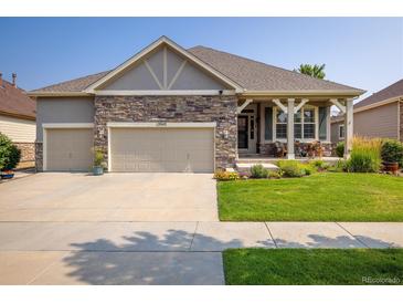 Charming home featuring a three-car garage, stone accents, and well-maintained landscaping with vibrant green lawn at 13943 W 87Th Ln, Arvada, CO 80005