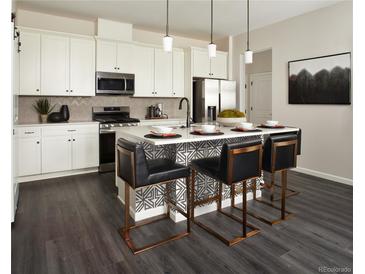 Bright kitchen features white cabinets, stainless steel appliances, and a large center island with counter seating at 6153 N Ceylon St # 205, Denver, CO 80249
