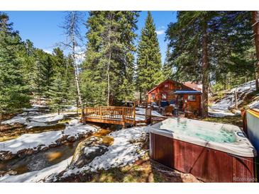Charming cabin with a bridge over a stream, complemented by a relaxing hot tub in a serene wooded setting at 27802 Shadow Mountain Dr, Conifer, CO 80433