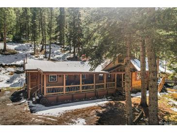 Inviting log cabin with a covered porch nestled among tall pine trees and snow at 27802 Shadow Mountain Dr, Conifer, CO 80433