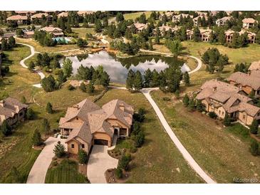 Stunning aerial view of a home with mature landscaping and a community pond at 5069 Castle Pines S Dr, Castle Rock, CO 80108
