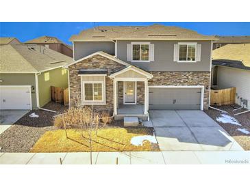 Charming home features stone accents, gray siding, a two-car garage, and manicured lawn at 885 Hearthstone Ave, Brighton, CO 80601
