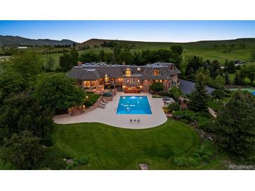 Aerial view of a luxury home featuring a stunning pool, lush lawn, and mature trees against a scenic landscape at 8000 N 41St St, Longmont, CO 80503