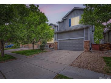 Charming two-story home with gray siding, stone accents, mature trees, and a two car garage at 12125 Helena St, Brighton, CO 80603
