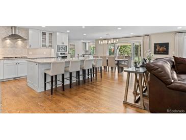 Bright, spacious kitchen with white cabinetry, an island with barstool seating, and hardwood flooring, open to dining area at 560 Front Range Rd, Littleton, CO 80120