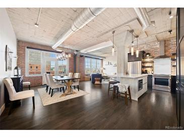 An open floor plan features a kitchen, dining and living area with exposed ceiling, brick accent wall and large windows at 1301 Wazee St # 3C, Denver, CO 80204