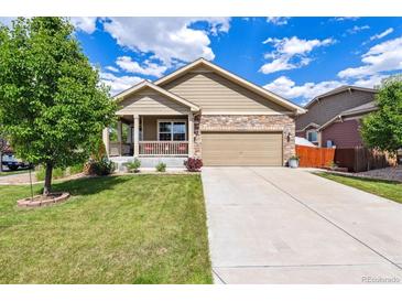 Charming home featuring stone accents, a covered porch, a well-manicured lawn, and an attached two-car garage at 10288 Olathe Way, Commerce City, CO 80022