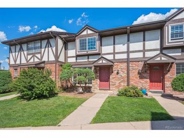 Charming townhome featuring brick facade, Tudor-style accents, manicured lawn, and inviting red front door at 3855 S Monaco St # 182, Denver, CO 80237
