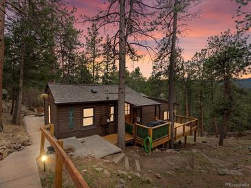 Charming cabin nestled among the trees, featuring a wooden deck and quaint exterior lighting at 4786 Forest Hill Rd, Evergreen, CO 80439