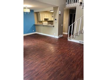 Open concept living room with wood floors that flow into the kitchen and stairway to the second floor at 14096 E Radcliff Cir, Aurora, CO 80015