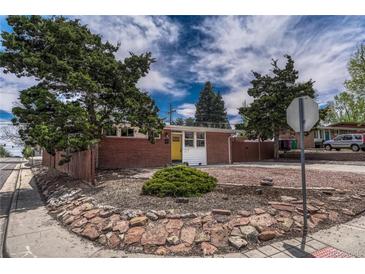 Charming brick home with a yellow front door, set back from the street with mature trees and landscaping at 1906 S Vrain St, Denver, CO 80219