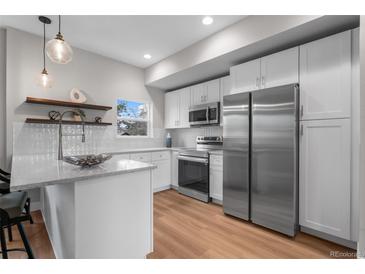 Bright kitchen featuring stainless appliances, white cabinets, granite countertops and wooden shelves at 2140 S Ash St # 102, Denver, CO 80222