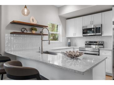 Modern kitchen features quartz countertops, stainless steel appliances, tile backsplash, and floating shelves at 2140 S Ash St # 102, Denver, CO 80222