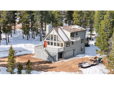 Charming mountain home with a striking red door, deck, and attached garage surrounded by a snow-covered landscape at 10747 Timothys Dr, Conifer, CO 80433