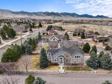 Stunning gray two-story home featuring a white fence, lush lawn, mature trees, and picturesque mountain views at 5753 Secrest Ct, Golden, CO 80403