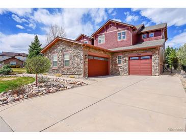 Inviting two-story home featuring stone accents, red siding, a spacious driveway and attached two-car garage at 7999 S Blackstone Pkwy, Aurora, CO 80016