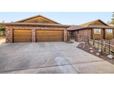 Charming brick home with a large concrete driveway and beautiful wooden garage doors at 8229 Red Rock Pl, Larkspur, CO 80118