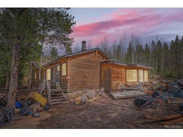 Rustic log cabin exterior with wooden steps and forested backdrop beneath a pink sunset sky at 1645 Little Bear Creek Rd, Idaho Springs, CO 80452