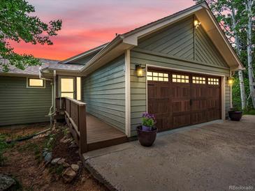 Charming home featuring a brown garage door, wood-paneled siding, and a sunset background at 30382 Kings Valley East, Conifer, CO 80433