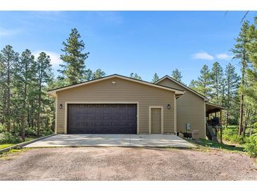 Attached two-car garage with dark wood doors and durable concrete driveway surrounded by natural landscape at 11044 Conestoga Pl, Franktown, CO 80116