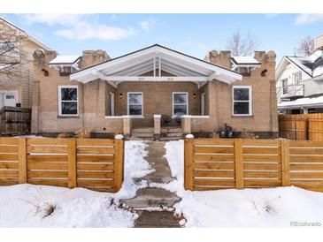 Charming brick home featuring a welcoming front porch and tidy snow-covered yard with a wooden fence at 2647 N High St, Denver, CO 80205
