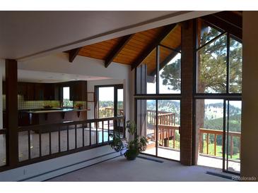 Bright living room featuring vaulted wood ceilings, exposed brick, and a wall of windows with a view at 21849 Cabrini Blvd, Golden, CO 80401