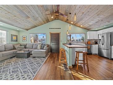 Open-concept living room and kitchen with wood-plank ceiling, stainless steel appliances, and breakfast bar with seating at 3270 Depew St, Wheat Ridge, CO 80212