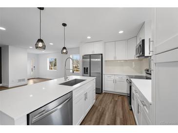 Bright, white kitchen features an island, stainless steel appliances, and modern pendant lighting at 5292 Columbine Ln, Denver, CO 80221