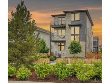 Beautiful modern three-story home with stone accents and balconies, complemented by professional landscaping and a charming picket fence at 21345 E 59Th Dr, Aurora, CO 80019
