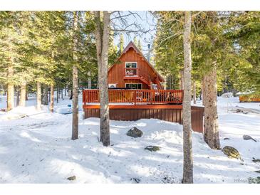 A-frame cabin with wrap-around deck and hot tub, nestled in a snowy wooded area at 381 Lake Rd, Idaho Springs, CO 80452