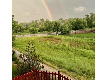 Rainbow over grassy backyard with red fence and trees at 15972 W 70Th Dr, Arvada, CO 80007